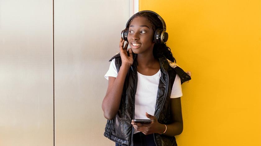 一个十几岁的女孩靠墙站着听耳机